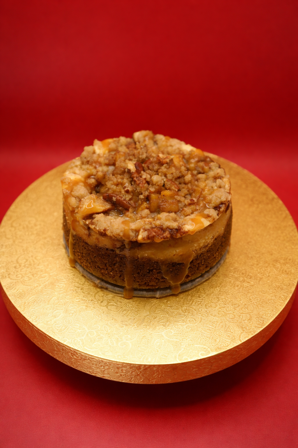 Cheesecake with crumbly topping on a gold plate against a red background